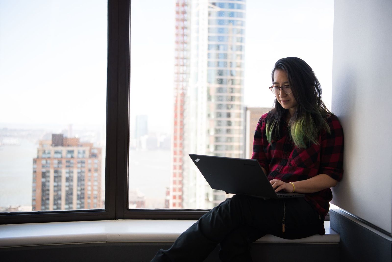 街を見下ろすオフィスの窓辺でノートPCを使う女性